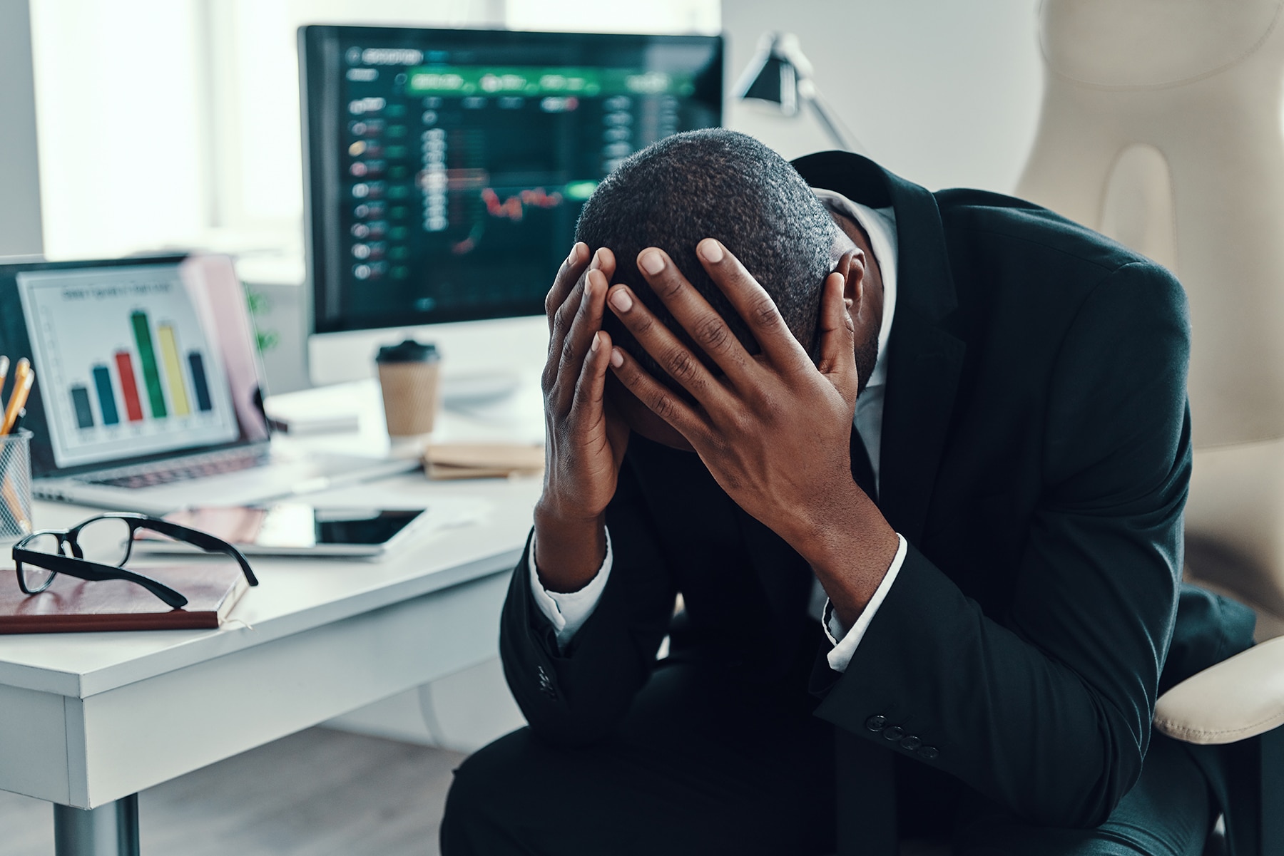 Tired young African man in formal wear keeping head in hands while working in the office